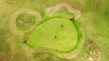 Üç adam bayrağı salladı ve uzaklaştı. Sporcular golf sahasında golf oynarlar. Üst görünüm.