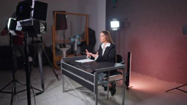 Masada oturan kadını aydınlatmaya hazır. Esmer kadın muhabir kamerayla konuşuyor..