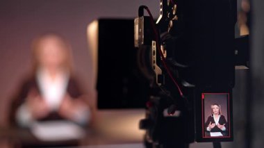 Tripodun üstündeki profesyonel kamera bir kadın muhabiri çekiyor. Bir programın ya da podcast 'in stüdyo görüntüleri. Bulanık arkaplan.