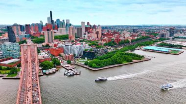 Tekneler East River 'dan Brooklyn Köprüsü' ne doğru hareket ediyor. Köprüden bir sürü araba geçiyor. New York şehir manzarasına hava perspektifi.