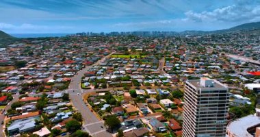 Güzel evleri ve yeşil caddeleri olan alçak katlı yerleşim alanının üzerinden uçun. Arka planda gökdelenler var. Honolulu, Hawaii, ABD.
