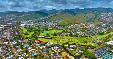 Palmiye ağaçları ve golf sahası olan güzel yeşil bir park. Sahne arkasındaki yemyeşil dağlardaki yerleşim yerleri. Honolulu, Hawaii, ABD. Hava görünümü.