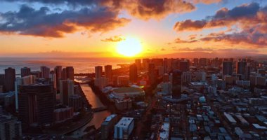 Gökyüzünde sersemletici batan güneş turuncu ve pembe bulutları aydınlatıyor. Honolulu, Hawaii, ABD hava kararınca insansız hava aracı uçuşu.