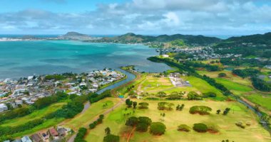 Ağaçlar büyürken golf sahasının üzerinde uçmak. Spor sahalarının çevresindeki yerleşim alanlarında alçak binalar. Oahu, Hawaii, ABD.