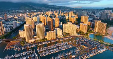 Çok sayıda tekneyle büyük yat kulübünün üzerinden uçmak. Parlak batan güneşin ışığında Waikiki manzarasında yüksek binalara yaklaşıyoruz. Honolulu, Hawaii, ABD.