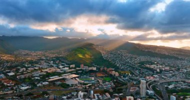 Batan güneş ışınları yeşil dağları aydınlatan yoğun bulutların arasından geçer. Gün batımında Honolulu, Hawaii, ABD manzarasına hava perspektifi.