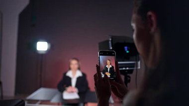 Telefon tutan ve arka planda bir bayanı çeken tanınmamış uzun saçlı kadın. Stüdyoda çalışan bir kadın muhabirin fotoğraflarını çekiyor..