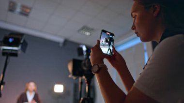 Kadın bir muhabirin videosunu çekiyor. Esmer kadın akıllı telefonuyla video kaydediyor. Düşük açı görünümü.