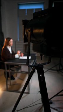 Profesyonel Soffit, fotoğraf stüdyosunda masa başında oturan kadına bakıyor. Kadın muhabir blog için video kaydediyor. Dikey video.
