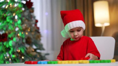 Şirin küçük çocuk masadaki oyuncaklarına bakıyor. Güzel bebek ayağa kalkar ve kaçar. Bulanık arkaplanda Noel ağacı.