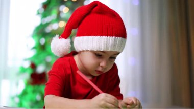 Kırmızı Noel Baba şapkalı güzel çocuk hobisine odaklanmış. Küçük çocuk pembe bir kalemle çiziyor..