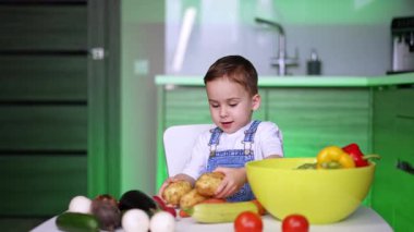 Kafkasyalı çocuk mutfakta sebzelerle oynuyor. Sevimli çocuk üç büyük patates seçiyor..