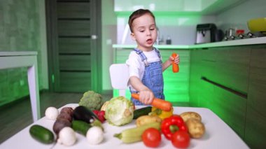 Kot pantolonlu sevimli çocuk elinde iki büyük havuç tutuyor. Bebek çocuk çeşitli sebzeleri işaret ederek onları öğreniyor..