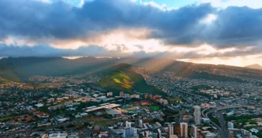 Kalın bulutlu hava, Honolulu, Hawaii, ABD manzarasını kapsıyor. Batan güneşin güzel ışınları bulutların arasından şehir manzarasına gider. Hava görünümü.
