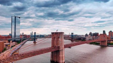 Çarpıcı Brooklyn Köprüsü 'nde araba ve insan akışı. Doğu Nehri üzerinde yükselen insansız hava aracı Manhattan Köprüsü 'nün arka plandaki görüntüsünü ortaya çıkarıyor. Bulutlu gökyüzü manzaranın üstünde.
