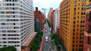 Yeşil ağaçlarla çevrili güzel şehir caddesi. Ulaşım akışının üzerindeki çok katlı binaların parlak cephelerindeki İHA görüntüleri. New York, ABD.