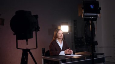Güzel, kendine güvenen beyaz bir bayan masasına oturmuş kamerayla konuşuyor. Kadın muhabirin yanında Soffit 'ler duruyor. Stüdyo görüntüleri.