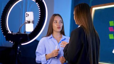 İki esmer kadın birbirleriyle aktif olarak konuşuyorlar ve ışık halkalarıyla kameraya dönüyorlar. Blog konsepti. Çevrimiçi akış.