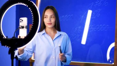 Güzel, beyaz bir kadın telefonun başında, ışık halkası ile görüntüler için bekliyor. Blogcu üzerine numara yazmak için cam duvara dönüyor.