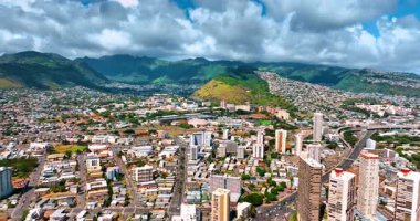 Yeşil dağlarla çevrili modern Honolulu, Hawaii, ABD 'nin engin manzarasının üzerinde uçuyor. Kayaların üzerinden güneşli şehirde dramatik bulutlar yükseliyor. Hava görünümü.