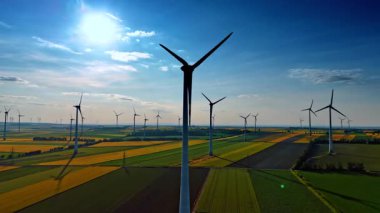 Yel değirmenleri mavi gökyüzünün arka planında döner. Rüzgâr çiftlikleri olan geniş tarlalar. Sürdürülebilir enerji üretimi.