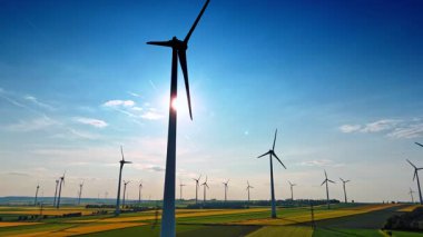 Rüzgarda dönen uzun rüzgar türbinlerinin siluetleri. Yeşil enerji üreten yel değirmenlerine düşük açı.