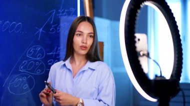 Çevrimiçi finans dersi eğlenceli! Parlak bir stüdyoda, video kalitesini arttırmak için beyaz tahta ve halka ışığı kullanan bir kişi finansal kavramlar öğretiyor..