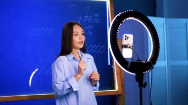 Genç bir kadın yüzük ışığının yanında poz veriyor. Mavi gömlekli genç bir kadın, mavi panodaki kavramları açıklarken, halka ışığının önünde güvenle konuşur..