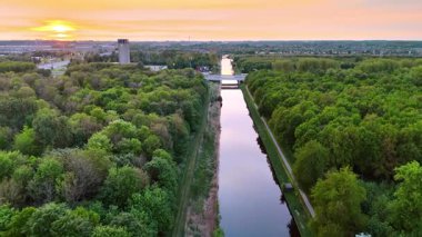 Bereketli yeşil manzarada gün batımı manzarası. Canlı bir günbatımı, sakin bir ortamda yoğun yeşillikle çevrili sakin bir kanala renkli yansımalar yapar..