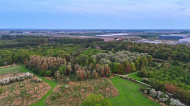 Şehir yeşilliği ve yakınlardaki tarlalar. Endüstriyel bir bölgeyi çevreleyen zengin bitki örtüsünün insansız hava aracı görüntüsü doğa ve gelişimin bir karışımını sergiliyor..