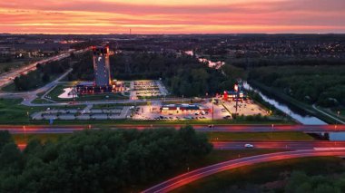 Şehir ve nehir üzerinde gün batımı. Canlı bir günbatımı gökyüzünü boyar, binaları, nehirleri ve arabalarla dolu yoğun yolları olan bir şehri yansıtır..