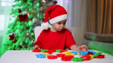 Çocuk parlak oyuncaklarla oynuyor. Kırmızı tişörtlü ve Noel Baba şapkalı bir çocuk festival dekorasyonları arasında renkli oyuncaklarla oynuyor..
