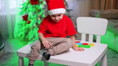 Çocuk kış eğlencesinde oynuyor. Bayram süslemeleri ile çevrili renkli etkinliklerle dolu bir masada oturan şenlikli bir çocuk..
