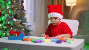 Çocuk tatille dalga geçiyor. Kırmızı elbiseli küçük bir çocuk renkli malzemelerle resim yapmayı, arka planda da şenlikli dekorasyonlar yapmayı seviyor..