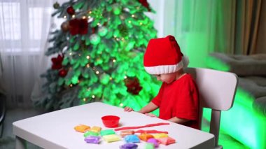 Noel zamanı evde çocuk işçiliği. Şenlik şapkası takan bir çocuk, tatil sezonunda renkli oyun hamuru şekilleri yaratmaya odaklanmış bir masada oturuyor..
