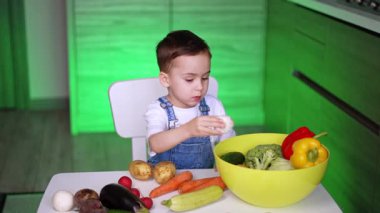 Mutfakta sebze keşfeden bir çocuk. Küçük bir çocuk taze sebzelerle çevrili bir masada oturuyor, ilginç bir şekilde büyük bir kaseyi inceliyor..