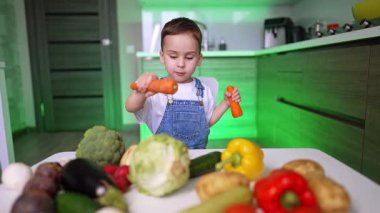 Renkli sebze oyunlarında oynayan bir çocuk. Genç bir çocuk canlı sebzelerle oynar, modern bir mutfak ortamında yaratıcılığını gösterir..