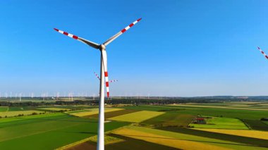 Rüzgar türbinleri temiz enerji üretir. Uzun rüzgar türbinleri uçsuz bucaksız yeşil ve sarı alanlar üzerinde açık bir gökyüzünde dönerek yenilenebilir enerjinin vaadini vurgular..