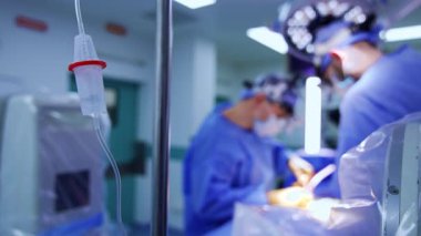 Salin solüsyonlu sayacı bırak. Kapatın. Bulanık zeminde iki erkek cerrah hastayı ameliyat ediyor..