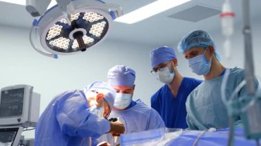 Modern ameliyathanede çalışan dört erkek doktor. Cerrahi hoparlörlerin başhekimi tıbbi cihaz uyguluyor..