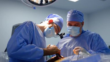 Cerrahi loplarda mavi üniformalı bir cerrah tıbbi alet uygular. Beyin ameliyatı yapan iki profesyonel beyin cerrahının görüş açısı düşük..