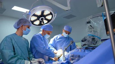 Modern ameliyathanede üç beyaz doktor ameliyat masasında duruyor. Beyin cerrahları beyin ameliyatı yaparlar. Düşük açı görünümü.