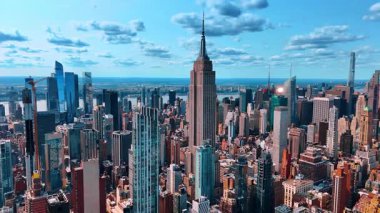 Empire State Binası, ABD 'nin New York kentsel manzarasından göze çarpıyor. Bulutlu gökyüzünün arka planında bir çan kulesiyle gökdelenin tepesine yaklaşıyoruz..