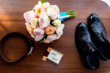 Düğün aksesuarları masaya serilmişti. Bir buket, ayakkabı, kemer ve kol düğmelerini de içeren bir düğün aksesuarı koleksiyonu..