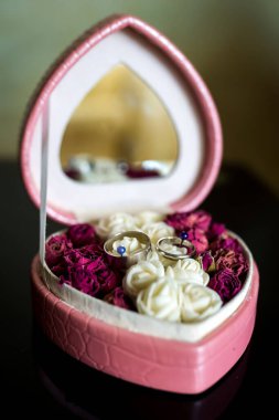 Çiçek yüzük kutusu tasarımı. Kurumuş gül ve yüzüklerle dolu zarif yüzük kutusu, karanlık bir yüzeyde sergileniyor, bir kutlama anını yakalıyor..