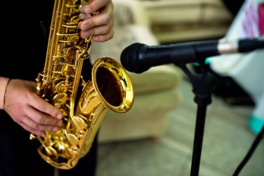 Saksafoncu mekanda çalıyor. Bir müzisyen, canlı bir iç mekanda mikrofonun yanında dururken altın saksafon çalar..