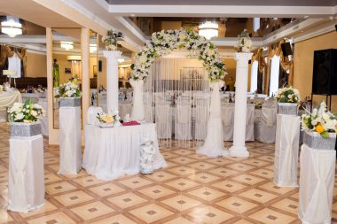 Bir ziyafet salonunda zarif bir düğün hazırlığı. Çiçeklerle süslenmiş güzel bir ziyafet salonu ve düğün için hazırlanmış bir kemer..