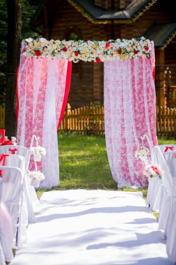 Güzel bir açık hava düğün töreni. Çiçeklerle süslenmiş bir kemer, misafirleri bahçede düzenlenen romantik bir düğün törenine davet ediyor..