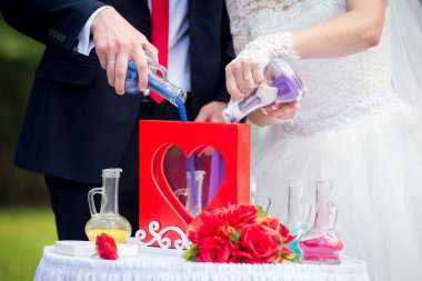 Renkli kumla birleşen çift. Bir gelin ve damat açık hava düğününde bir kalp şeklindeki konteynıra renkli kum döker..