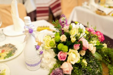 Çiçek süsü masanın üstünde. Renkli bir çiçek süsü, güller ve yeşillikle bir kutlama sırasında zarif bir yemek masasını süslüyor..